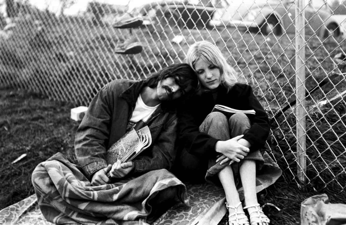 A Man And Woman Sitting On The Ground Next To A Fence