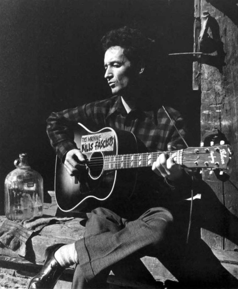 “Folk Music Legend - Woody Guthrie strumming his guitar on a bustling street" Wallpaper