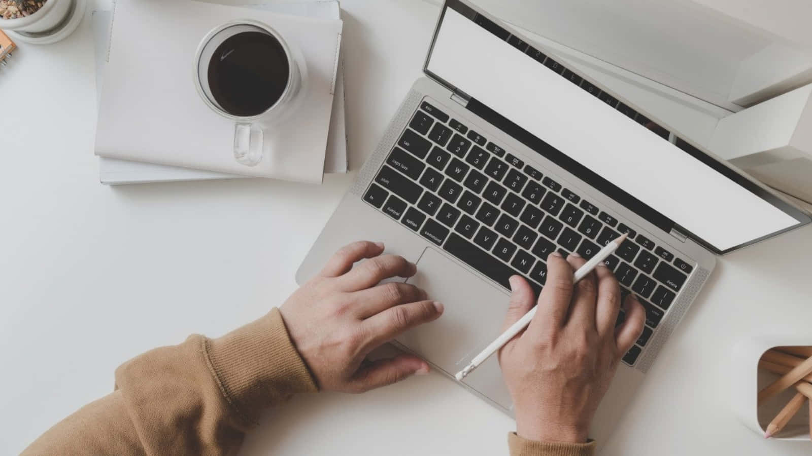 A Person Typing On A Laptop With A Cup Of Coffee