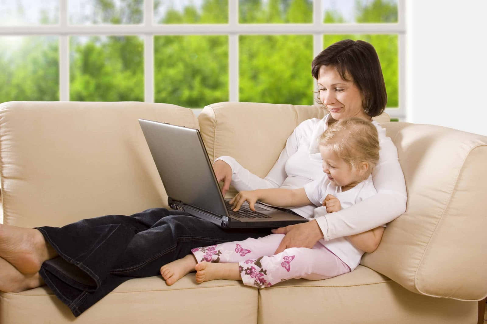 A Woman And Child Sitting On A Couch With A Laptop