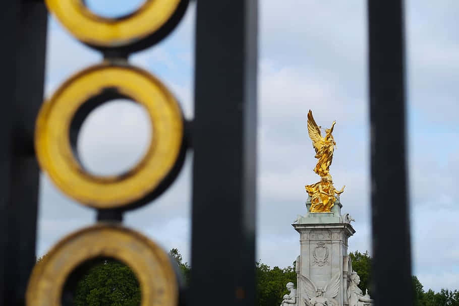 Buckinghampalaces Gyllene Staty Syns Genom Ett Staket På Dator- Eller Mobilskrivbordet. Wallpaper