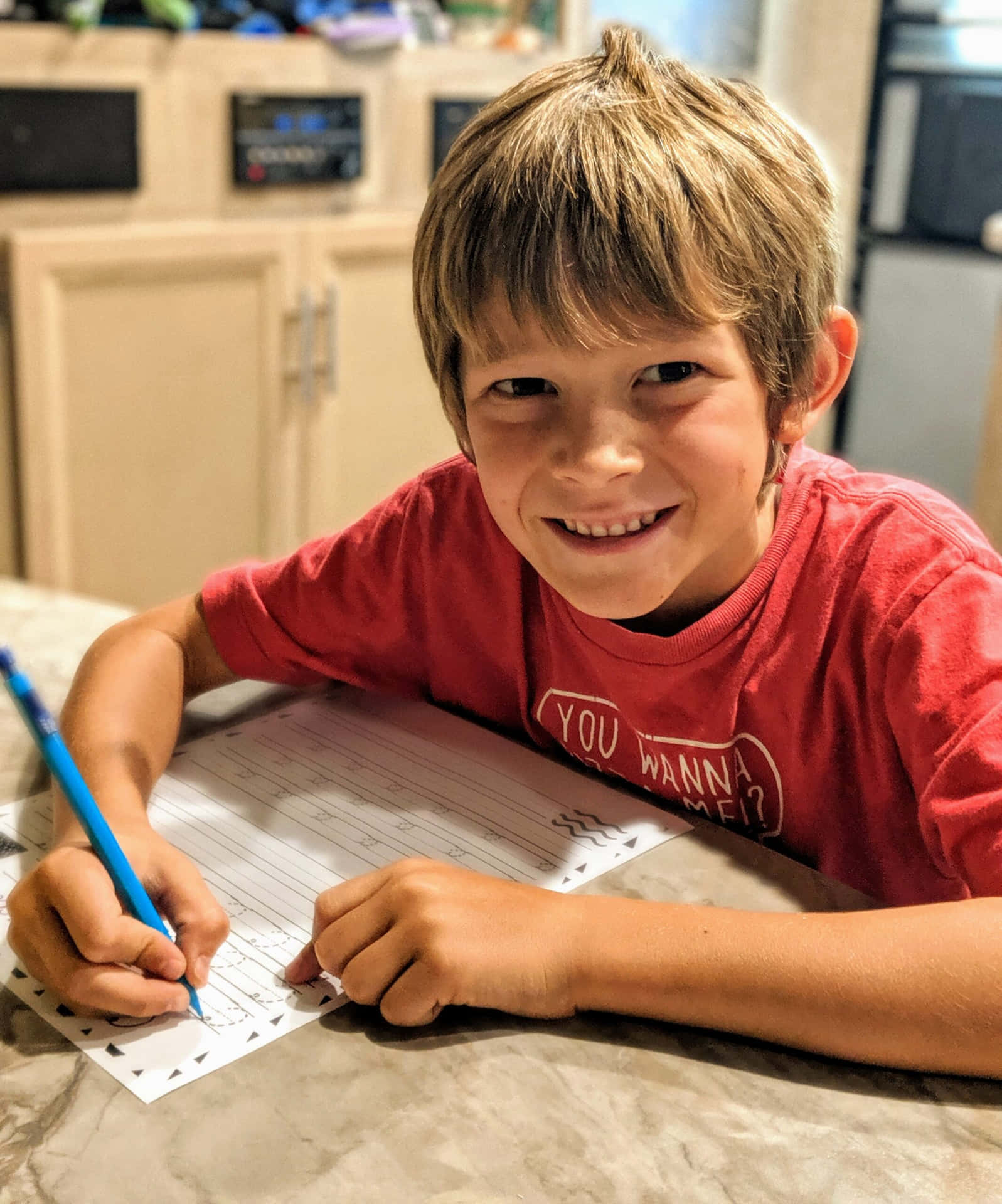 A Boy Smiling While Writing On A Piece Of Paper