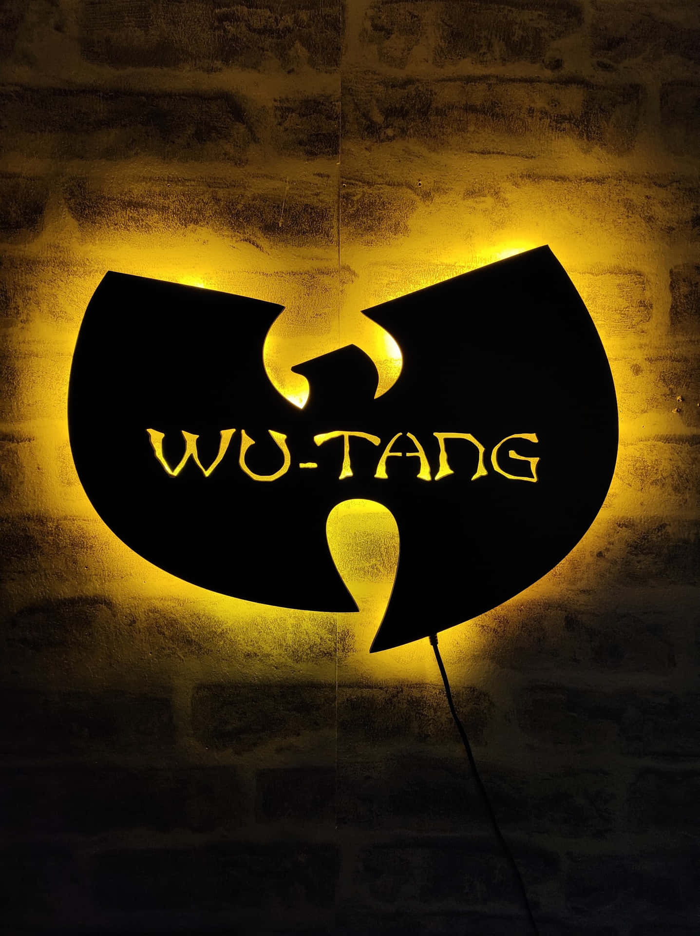 A Wutang Logo Is Illuminated On A Brick Wall Wallpaper