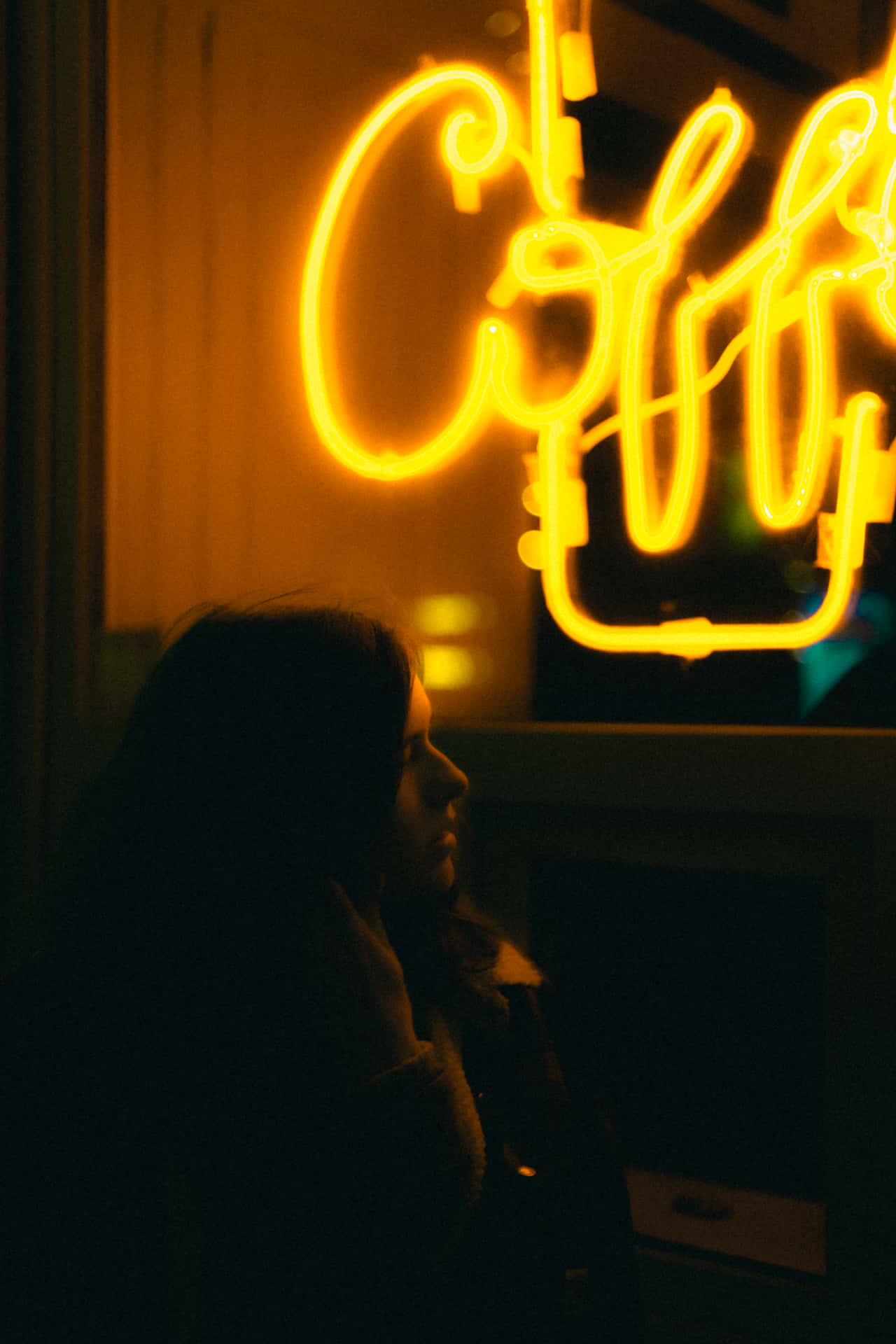En kvinde sidder foran et neon skilt Wallpaper