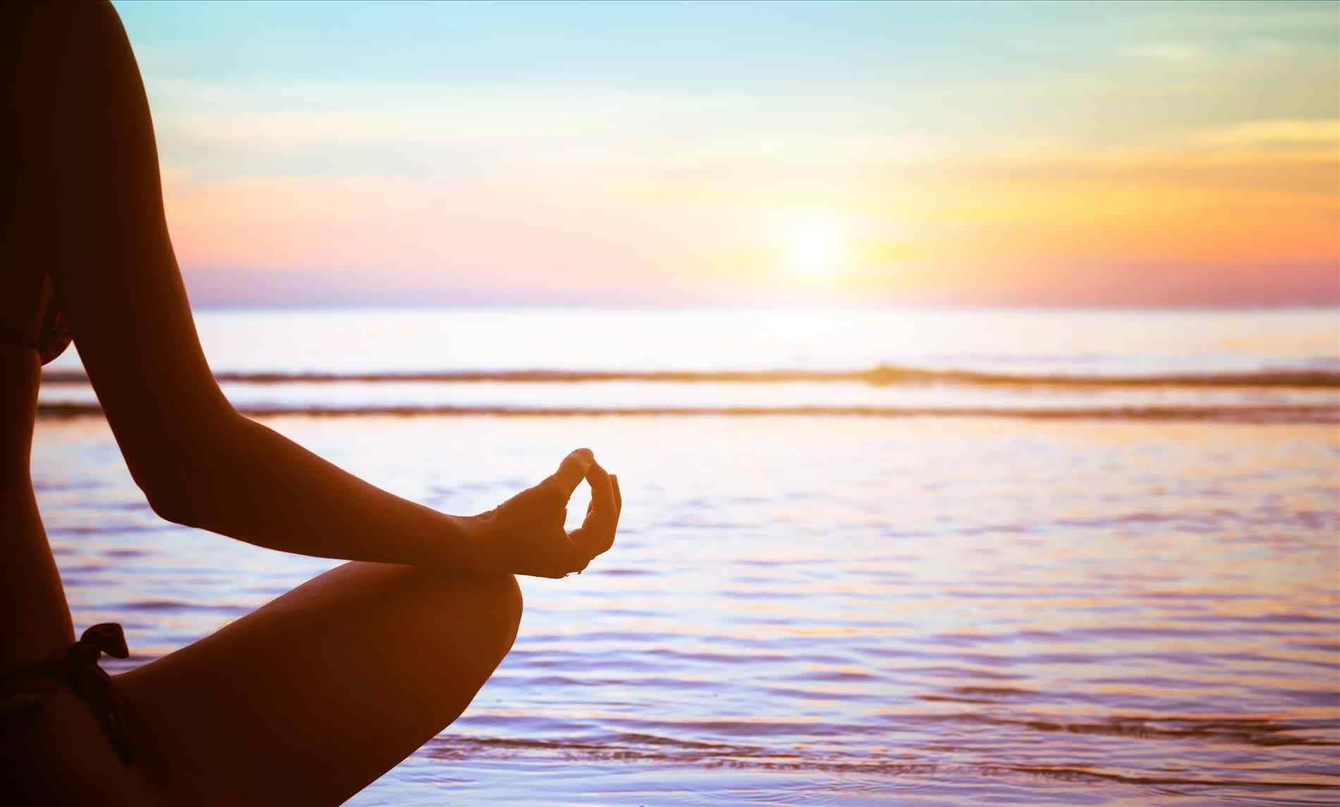 A Woman Is Meditating On The Beach At Sunset