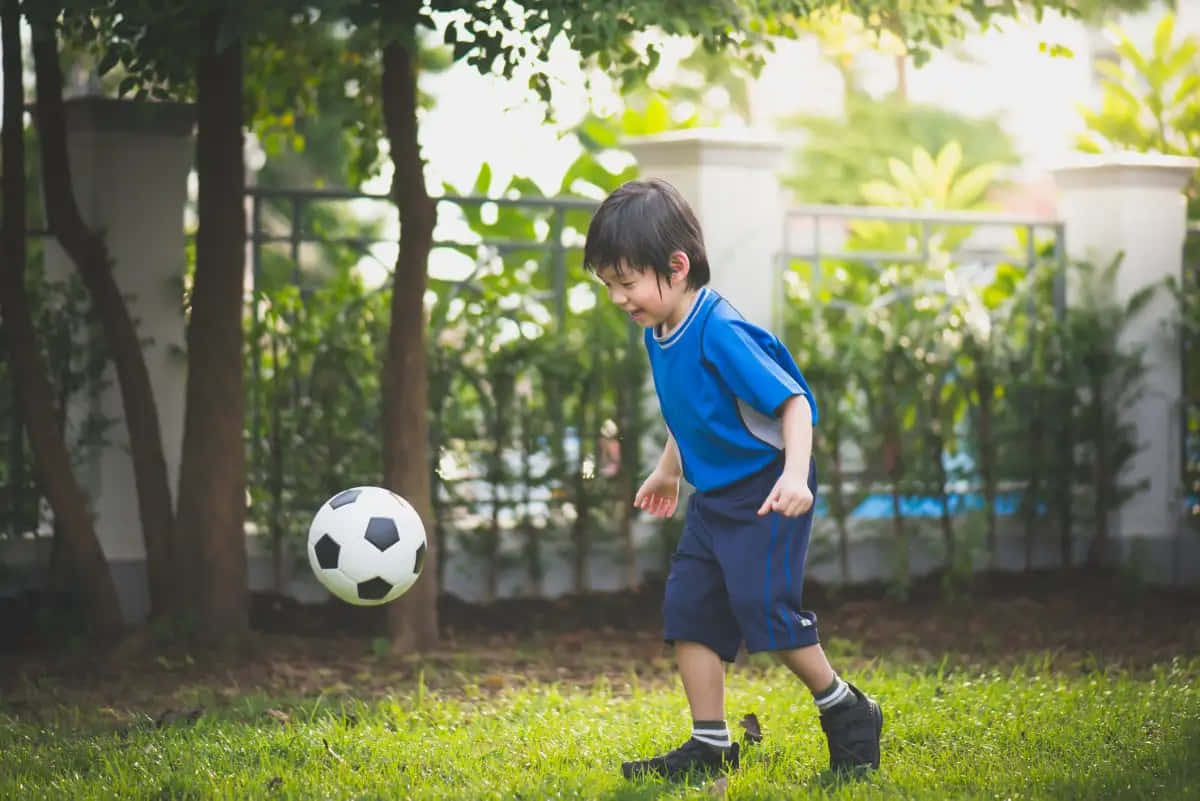 Young Boy Playing Soccerin Garden.jpg Wallpaper