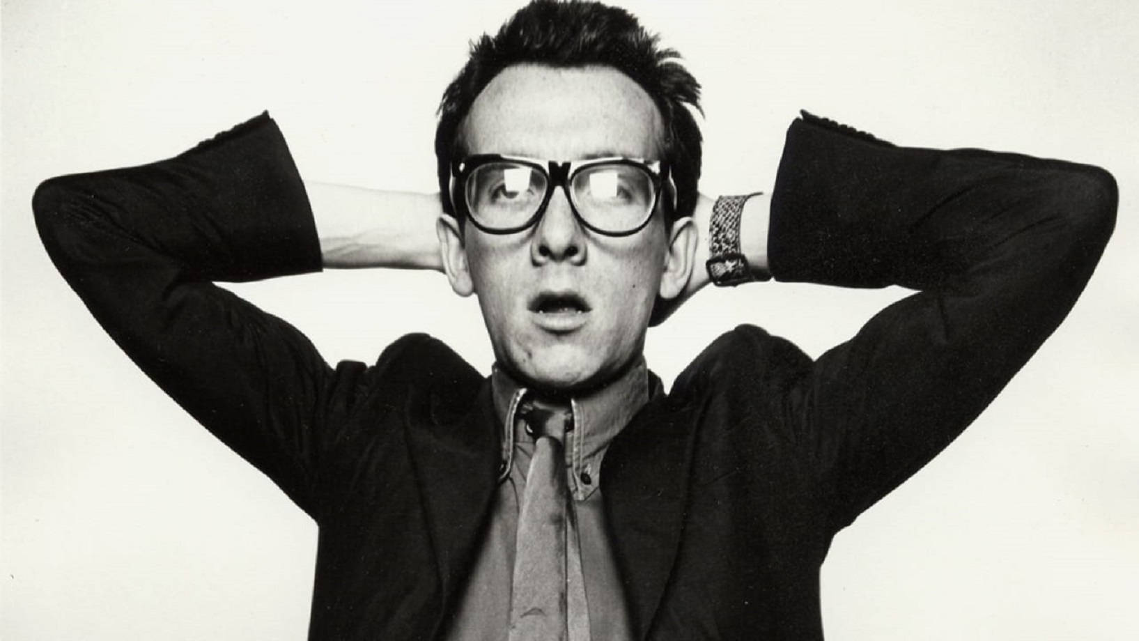 Caption: Young Elvis Costello Sporting His Iconic Nerd Look Wallpaper