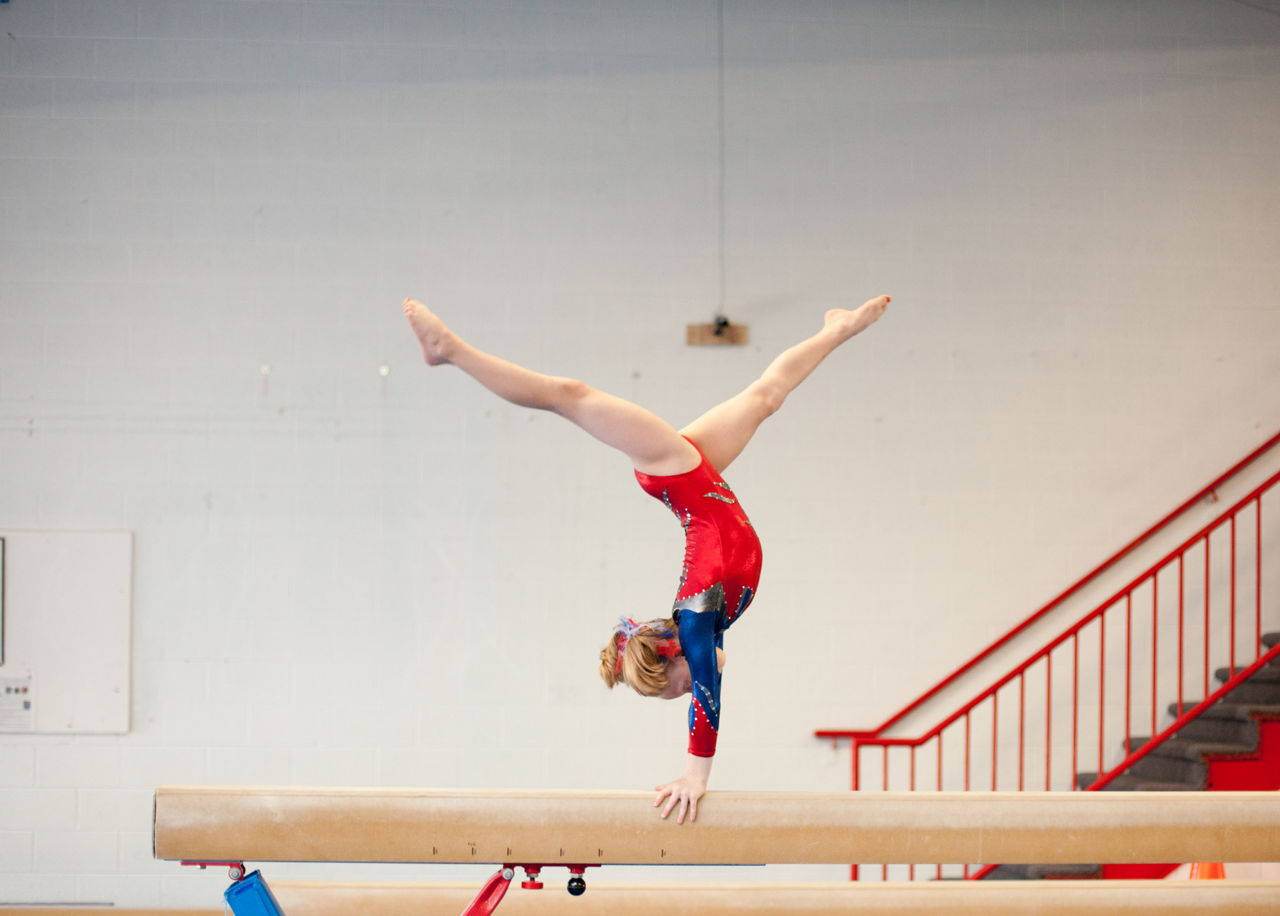 Young Gymnast In Handstand Split On Balance Beam Wallpaper