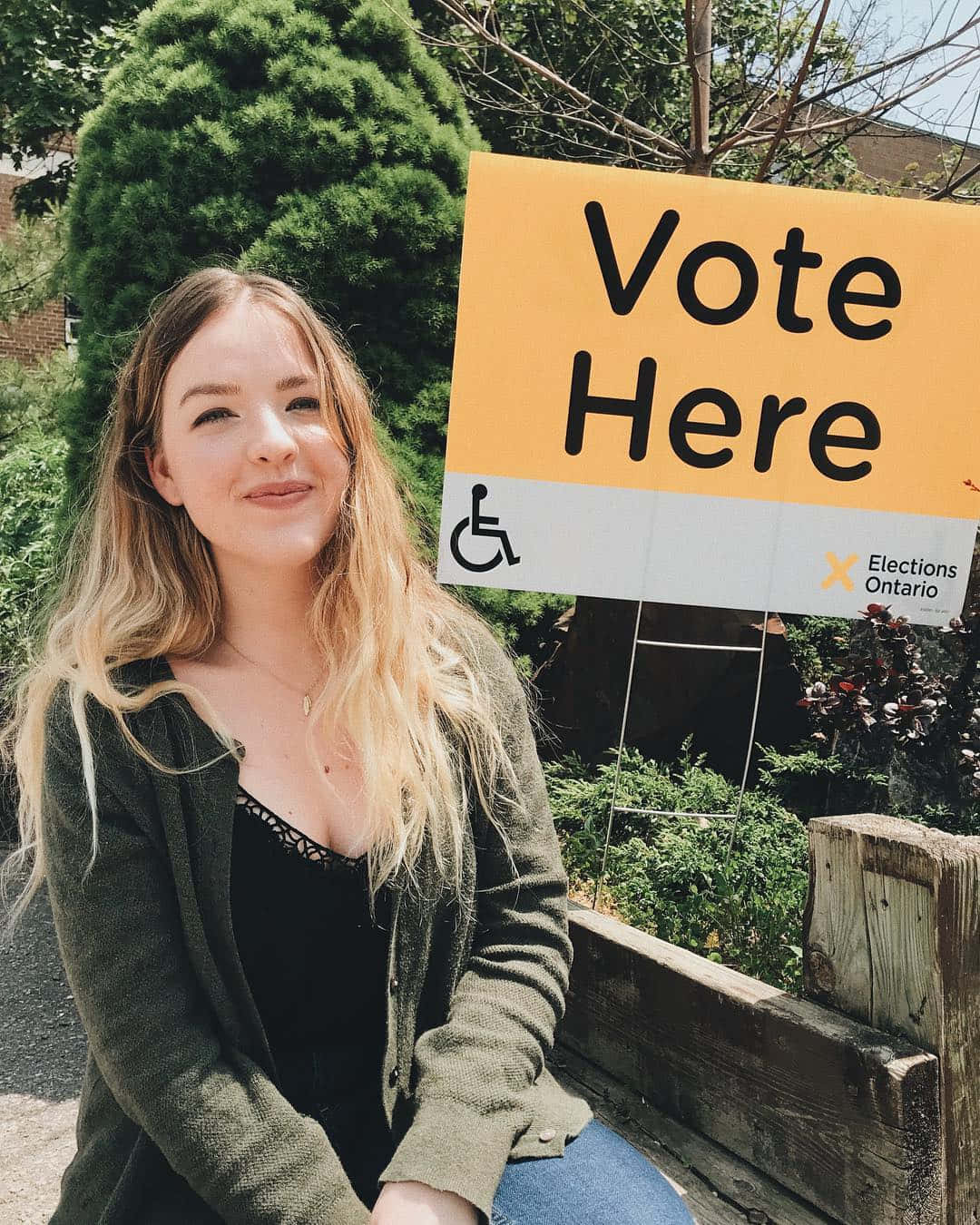 Young Woman Smiling Near Vote Here Sign Wallpaper
