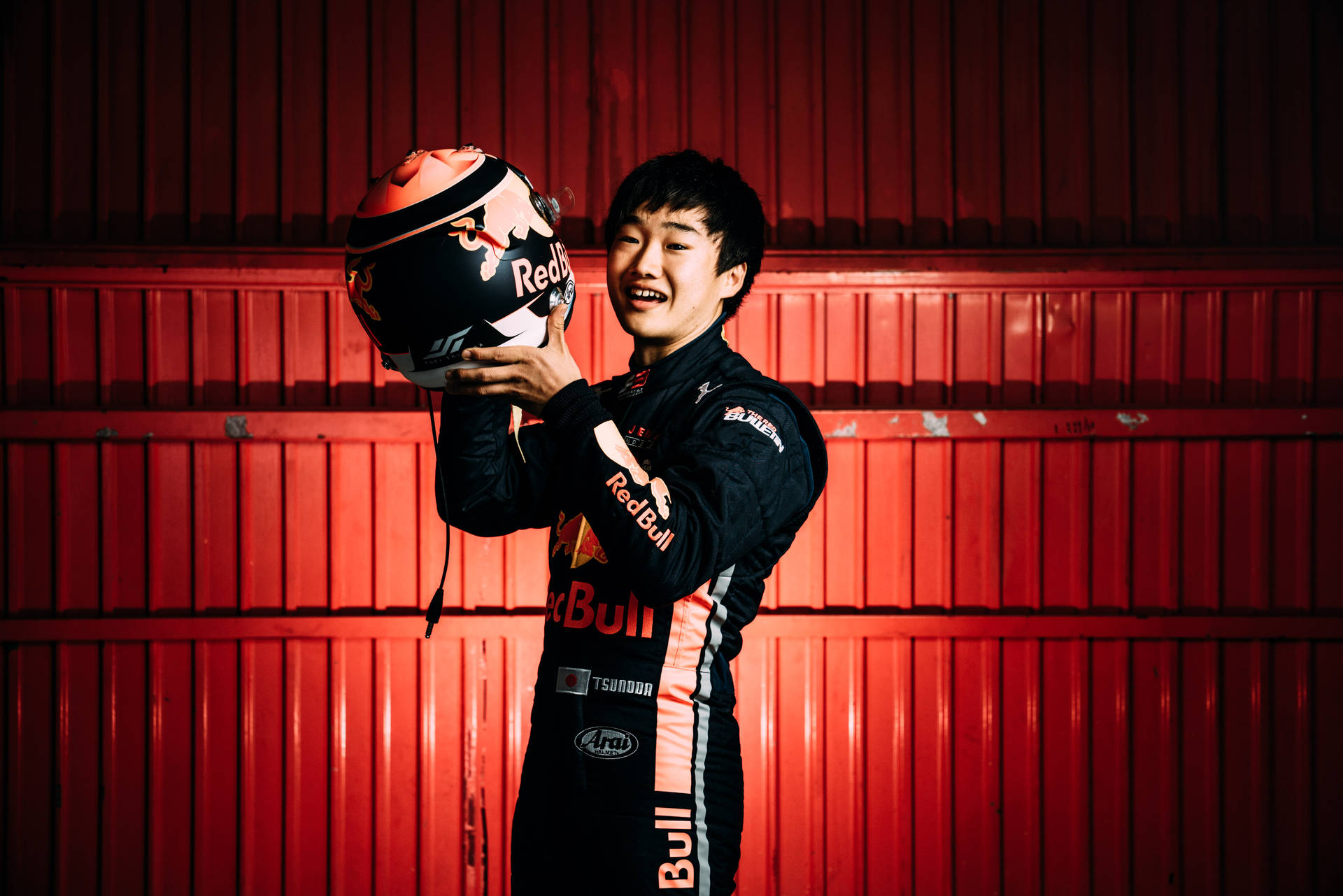Caption: Yuki Tsunoda, with a Bright Smile, Holding His Helmet. Wallpaper