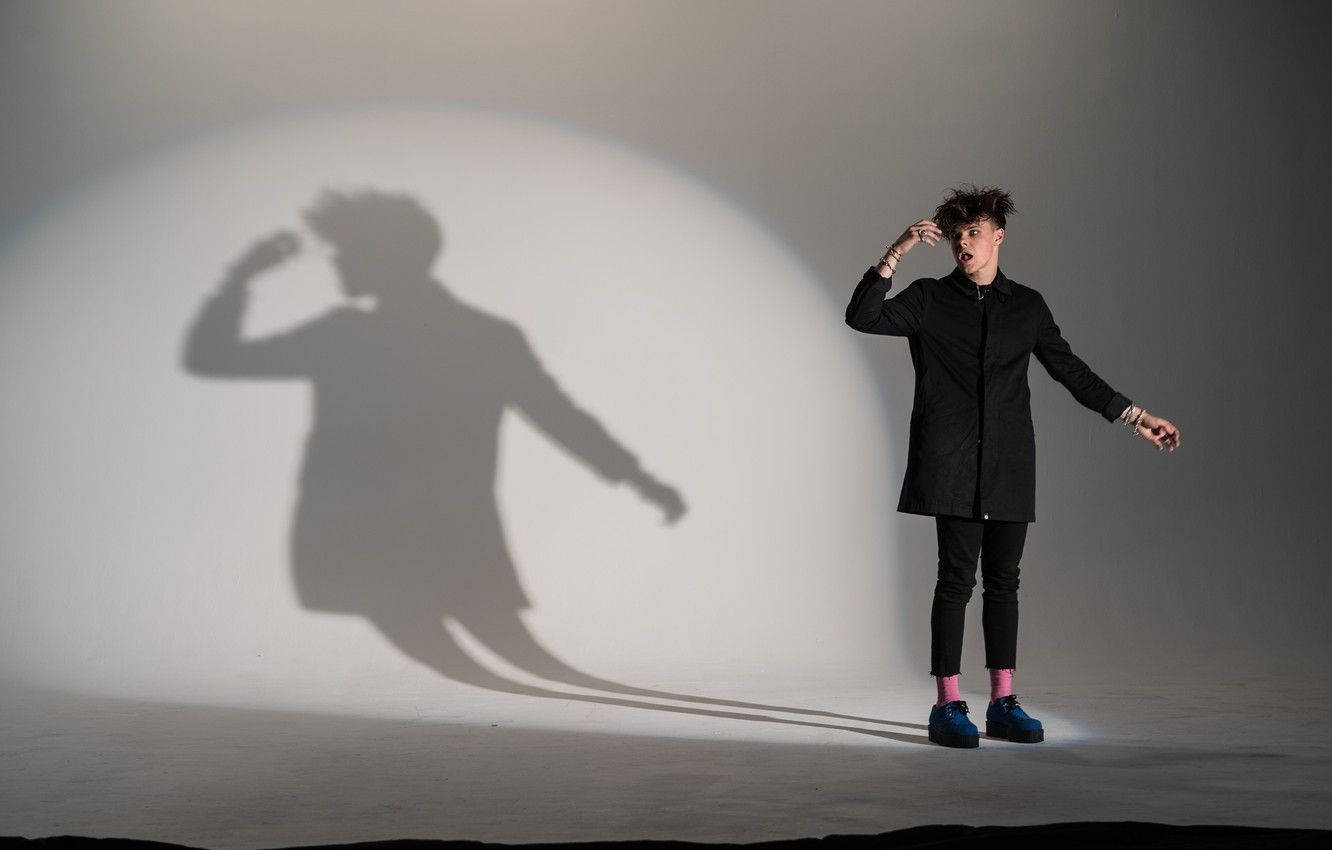 a man in a black coat standing in front of a shadow Wallpaper
