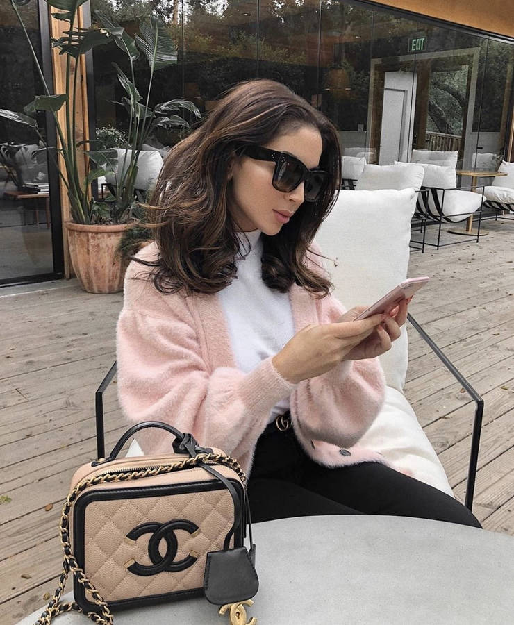 En kvinde sidder på en bænk med en pink sweater og Chanel-taske.