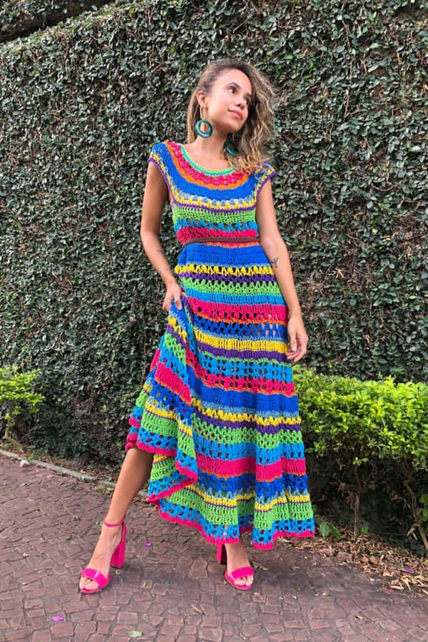 umamulher em um vestido de crochê colorido posa na frente de uma parede.