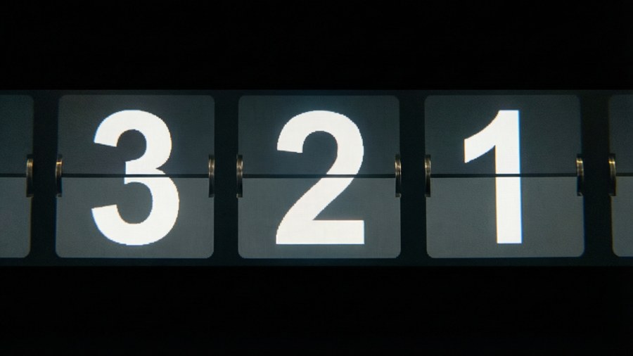 Une horloge à palettes mécanique montrant les chiffres du compte à rebours 3 2 1 en blanc sur un fond noir.