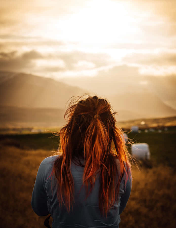 EineFrau mit roten Haaren, die über ein Feld schaut.