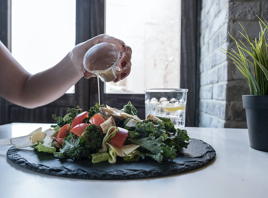 GrünerBlattsalat Hintergrundbilder — Ein Bild einer Person, die ein Dressing auf einen grünen Blattsalat gießt, der auf einem ästhetischen schwarzen Teller serviert wird.