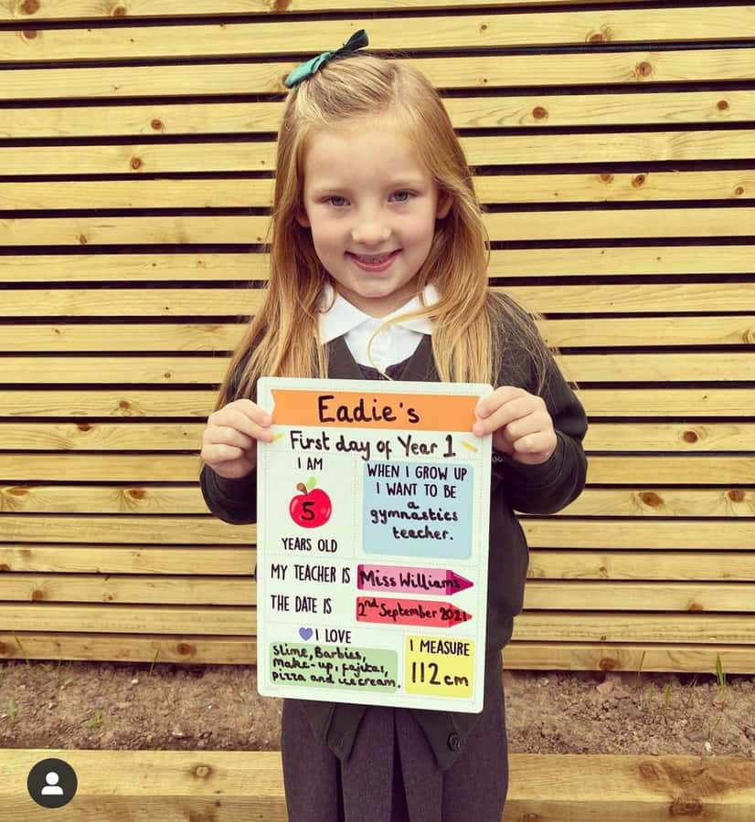 EinMädchen hält ein Schild hoch, auf dem steht "Edwards erster Schultag".