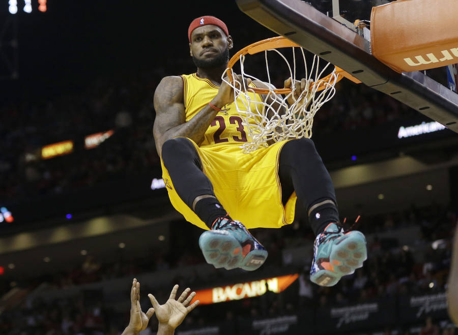 Lebron James in NBA Cavs 23 jersey hanging from a basketball ring wallpaper