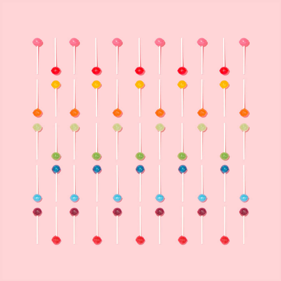 Minimal wallpaper of rainbow-colored lollipops on pink surface