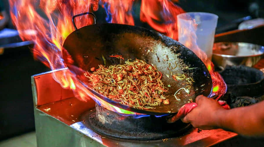 EinePerson kocht Essen in einem Wok auf dem Feuer.
