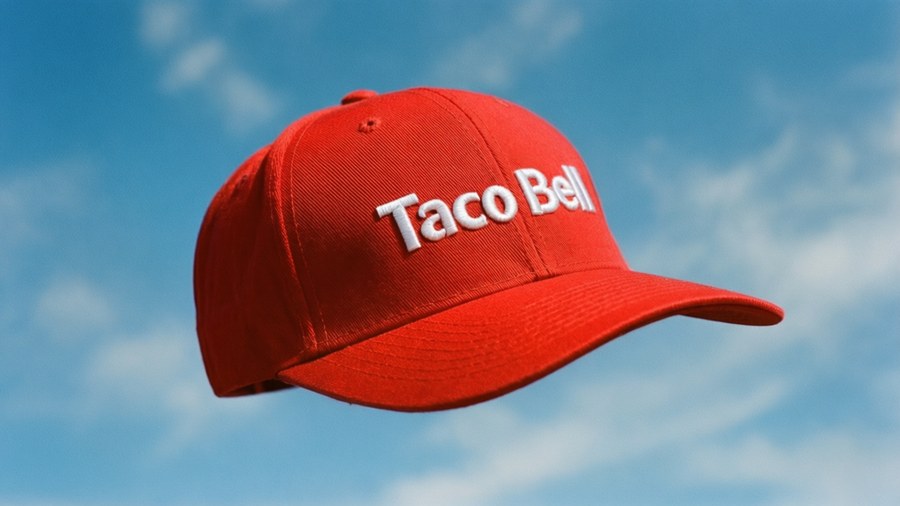 Floating red Taco Bell snapback hat with white text against blue sky.