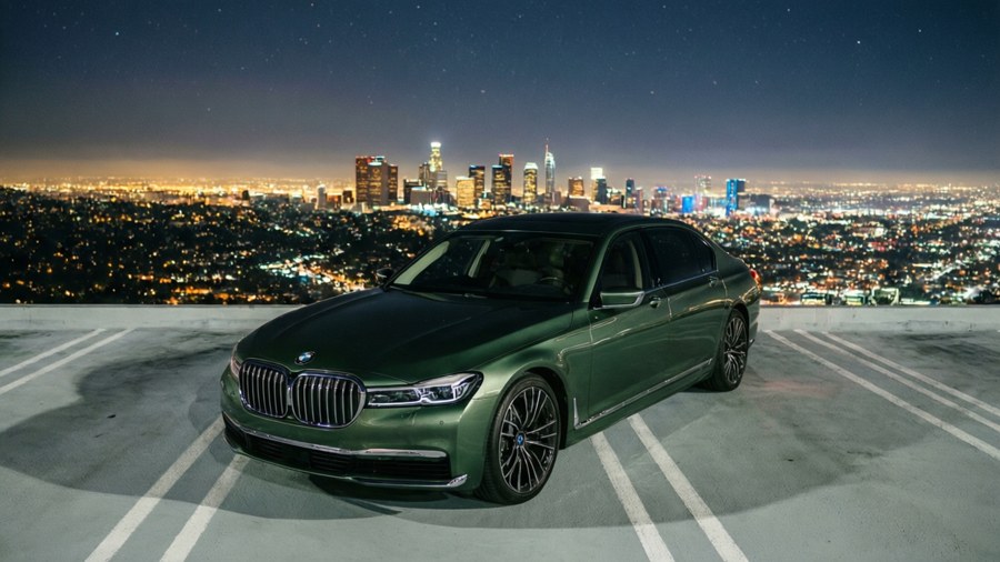Green BMW 7 Series on a rooftop parking at night with city skyline.