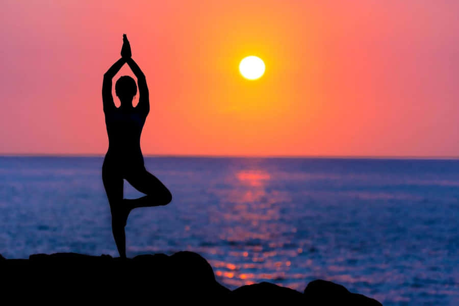 EineFrau praktiziert Yoga auf einem Felsen bei Sonnenuntergang.