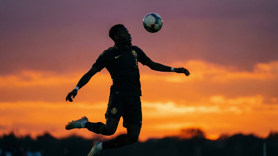 Silhouette of Benjamin Mendy heading a ball against a colorful sunset.
