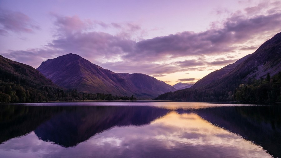 Een rustig landschap met violette bergen en paarse zonsonderganglucht, perfect voor een kalme achtergrond.