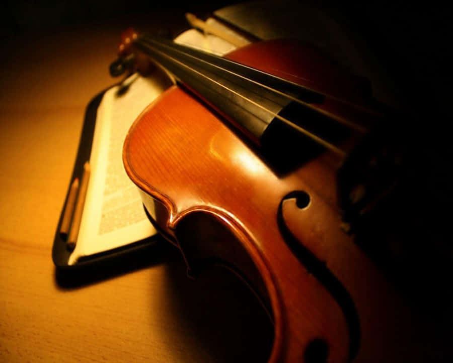 a violin is sitting on a table with an open book Fonds d'écran