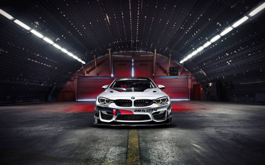 Hvit BMW M4 GT4 racerbil parkert i en hangar bakgrunn