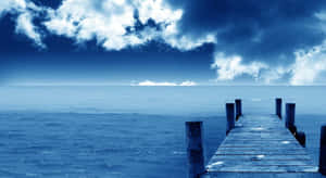 Un largo muelle de madera se extiende hacia aguas azules tranquilas bajo un cielo nublado. — Fondods de naturaleza en la computadora Fondos de pantalla