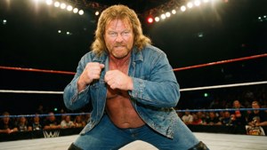 Hillbilly Jim in una posa dinamica di wrestling durante un evento WWE del 2006, folla sullo sfondo.