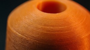 Makrokuva 3D-tulostetusta esineestä, jossa näkyy kerrosviivoja lämpimässä oranssissa valossa.
