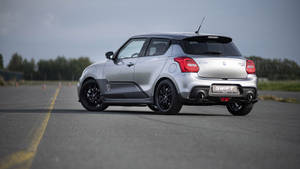 Silver Suzuki Swift sports car on an asphalt track with trees in background.