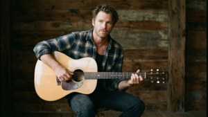 Daniel Gillies avec une guitare dans un cadre rustique.