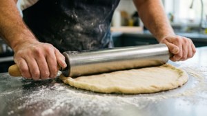 Et actionbilde av en baker som bruker en kjevle i rustfritt stål på paideig.