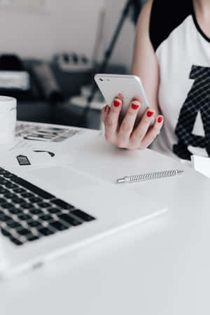 Close-up da mão de uma pessoa segurando um telefone em uma mesa branca com um laptop. — Desktop Android Papéis de Parede