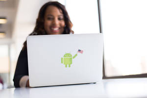 Woman smiling behind laptop with Android mascot holding American flag sticker. — Indie Aesthetic Laptop Wallpaper
