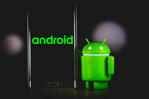 Figura verde do mascote Android ao lado de smartphone mostrando logotipo do Android em fundo escuro com luzes bokeh. — Natureza do Android Foto Papéis de Parede
