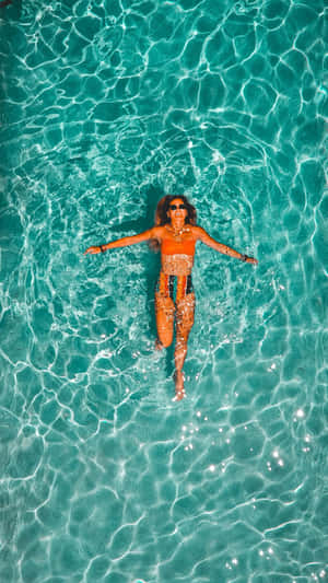A woman floating on her back in clear turquoise water wearing sunglasses and an orange swimsuit.