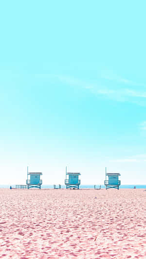 Three lifeguard towers on a pink beach under a clear blue sky.