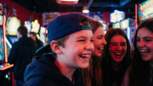 Uformelt øyeblikksbilde av gutt som ler med venner i neonlys arkade.