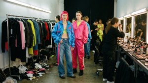 Models in colorful tracksuits pose backstage during a fashion show.