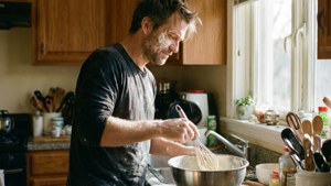 A person trying to bake in a cozy kitchen, with flour on face and sunlight.