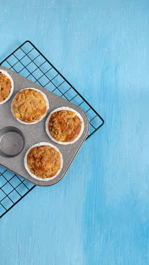 Four golden muffins with crumb topping cooling on a wire rack over a blue surface. — Baking iPhone Picture
