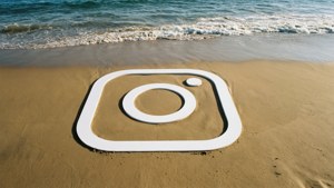 Weißes Instagram-Logo in den Sand am Strand geritzt, mit Wellen im Hintergrund