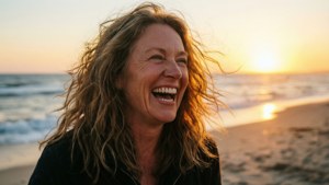 Kathleen Robertson griner ubekymret på stranden under en smuk gylden solnedgang.