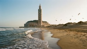 Mezquita Hassam II desde la playa con dunas y gaviotas, luz de la tarde.