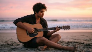KJ Apa spiller gitar på stranden ved daggry, rolig og fredelig.
